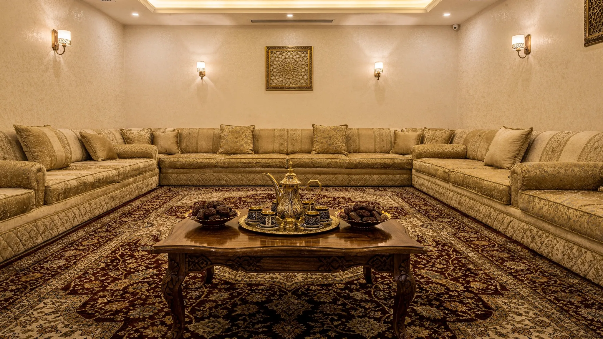 مجلس سعودي أنيق يضم كنباً مريحاً وسجادة فاخرة وطاولة خشب منخفضة في المنتصف مع فناجين قهوة وتمور وإضاءة دافئة